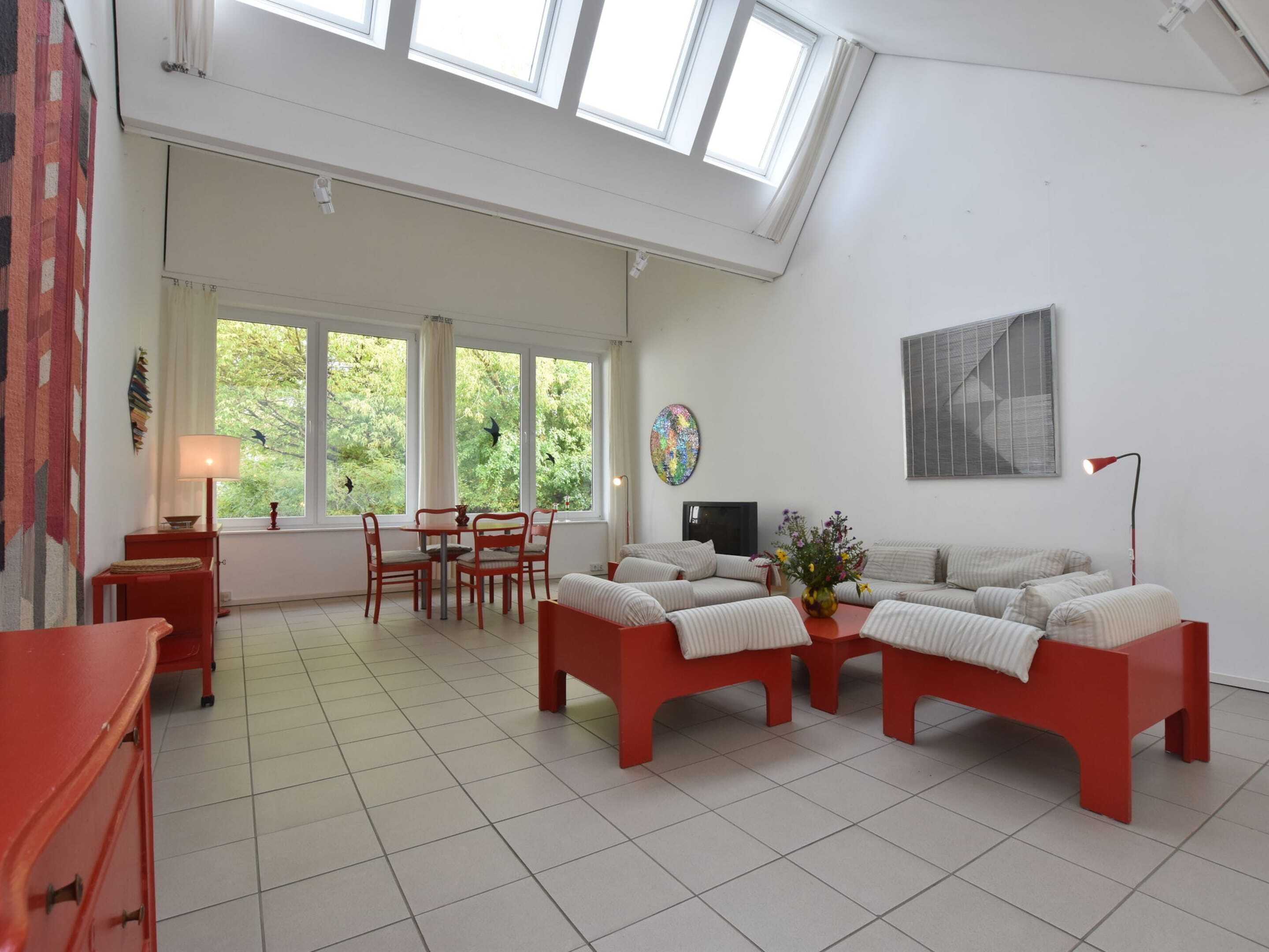 Un salon spacieux avec un plafond haut, de grandes fenêtres, un coin repas et un ensemble de canapés.