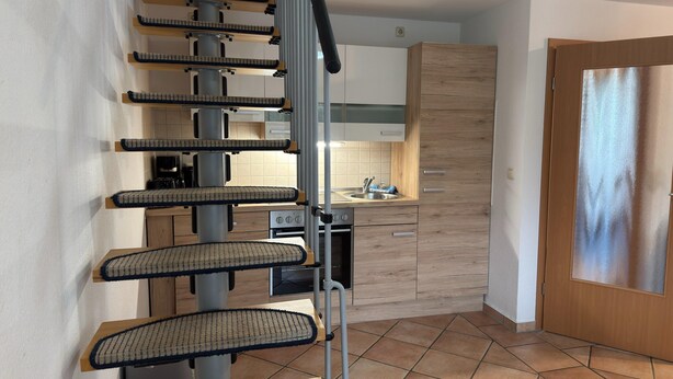 A modern kitchen with a wooden cabinet, a sink, and a staircase with a cat tree. - Graal-muritz Garden Balcony Stay (Graal Mueritz)