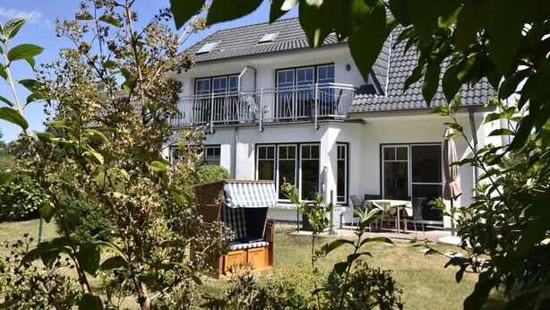 A two-story house with a balcony, a garden with a chair, and a table. - Graal-muritz Garden Balcony Stay (Graal Mueritz)