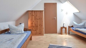 A bedroom with two wooden beds, a wardrobe, a door, and a small table. - Graal-muritz Garden Balcony Stay (Graal Mueritz)