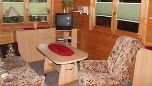 En mysig stuga med träpanel på väggarna, en tv, ett litet bord, en blommönstrad soffa och en klocka på väggen.