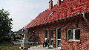 A red brick house with a sloped roof, a stone structure in the front yard, and a patio with chairs. - Spacious Holiday Home in Zierow near Sea (Zierow)