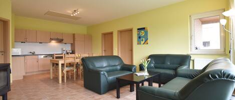 A living room with a dining area, kitchen, and a window with curtains.