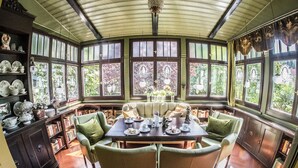 A sunroom with a large table, four chairs, and a view of the garden through large windows. - Timeless Charm in Gernrode (Quedlinburg)