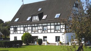 A traditional half-timbered house with a sloped roof, multiple windows, and a well-maintained lawn. - Wohnung in Silbecke mit Garten (Attendorn)