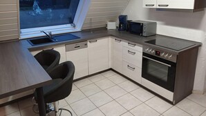 A compact kitchen with a window, a sink, a toaster, a microwave, and an oven. - Wohnung in Silbecke mit Garten (Attendorn)