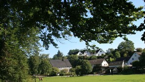 A rural landscape with a green field, a wooden fence, and houses in the background. - Wohnung in Silbecke mit Garten (Attendorn)