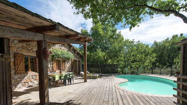 A wooden deck with a pool, outdoor furniture, and a stone building with windows. - Holiday Home in Ardeche With Pool (Saint Alban Auriolles)