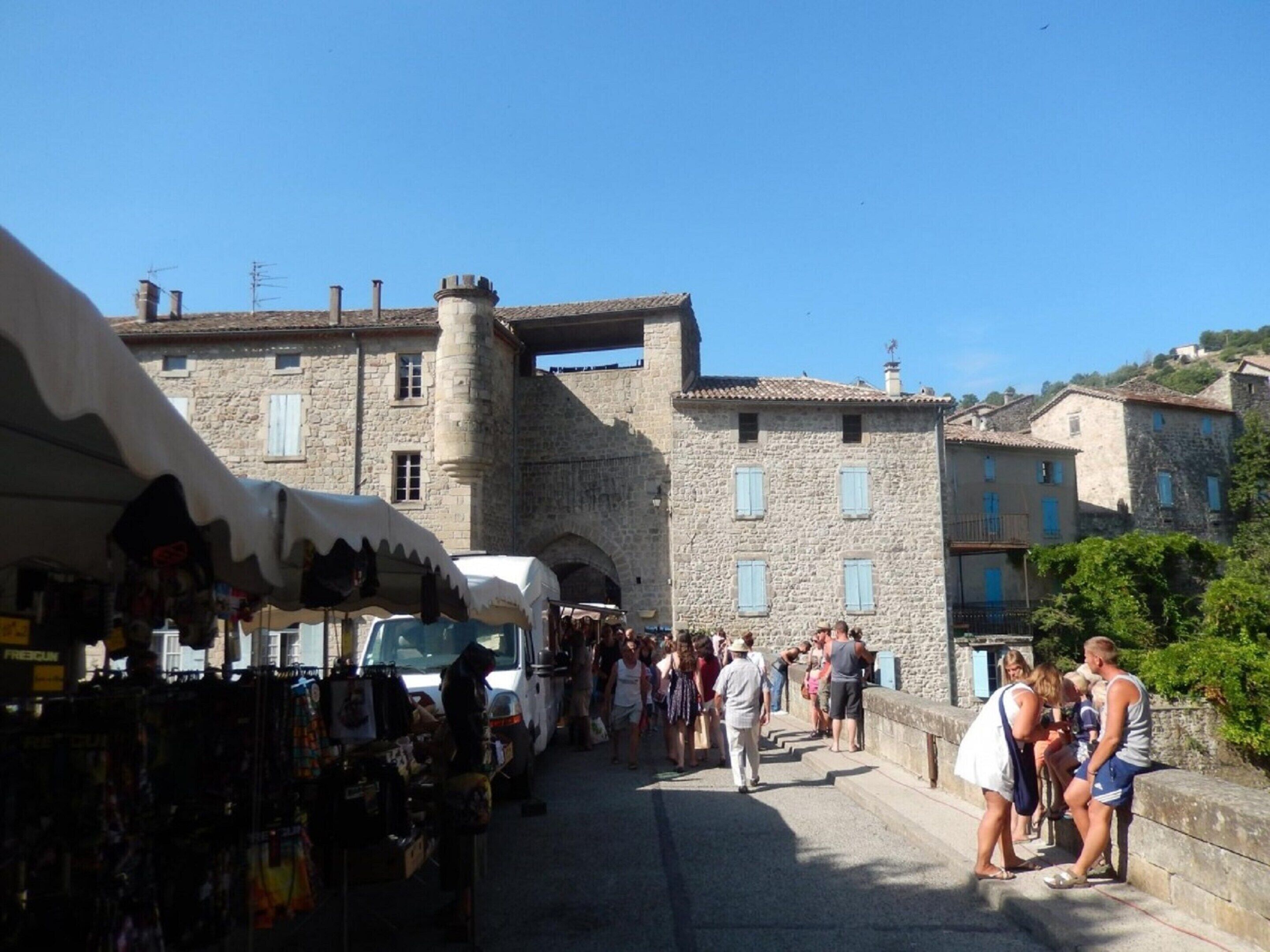 A stone building with a tower, a market area with stalls, and a crowd of people.