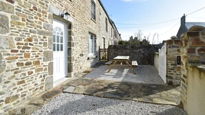 A stone building with a gravel courtyard, a wooden table, and a white door. - Quiet Normandy Retreat (La Haye)