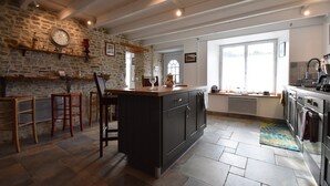 A kitchen with a stone wall, wooden bar stools, a central island, and a large window. - Quiet Normandy Retreat (La Haye)