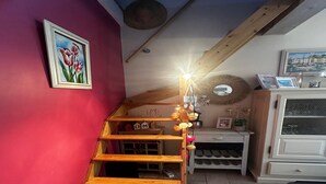 Eine Holztreppe mit einer Leuchte, eine rote Wand mit einem Tulpenbild und ein weißes Schränkchen mit Weinkühler.