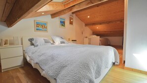 Ein Schlafzimmer mit Bett, Holzbalkendecke, Nachttisch und Kommode.