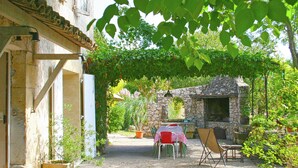 An outdoor patio area with a stone wall, a table with chairs, and potted plants. - Holiday Home in Provence With Private Pool (Cavaillon)