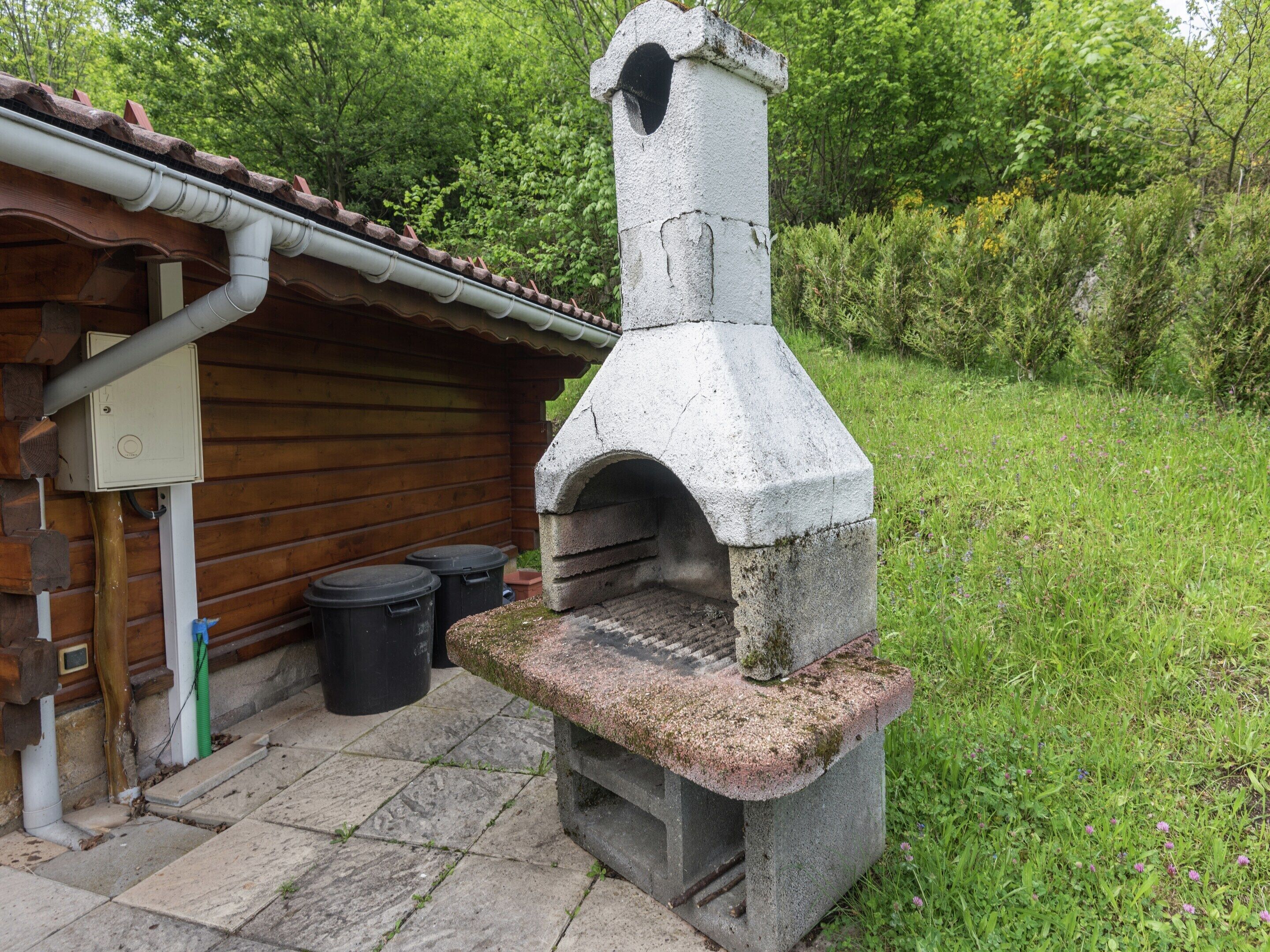 A stone-built outdoor oven attached to a wooden cabin with a tiled roof.