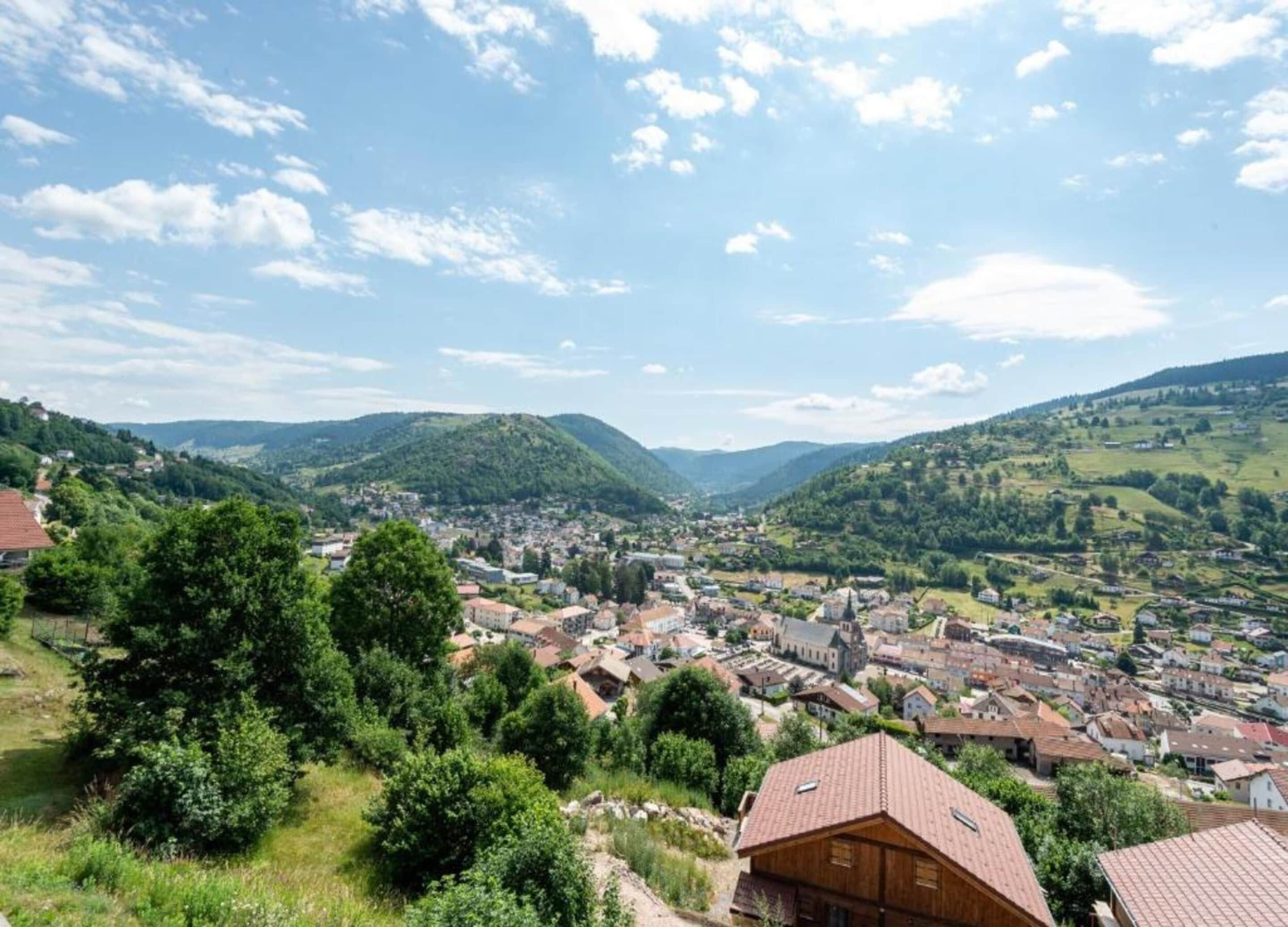 Une ville nichée dans une vallée, où se côtoient des bâtiments traditionnels et modernes, entourée de collines verdoyantes et sous un ciel dégagé.