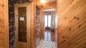 Ein Holzflur mit strukturiertem Wandpapier, gefliestem Boden und einer Tür zu einem Zimmer mit Bett und Vorhängen.