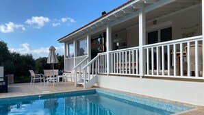 Ein Swimmingpool mit überdachter Terrasse, Gartenmöbeln und einer Treppe zu einer erhöhten Dachterrasse.