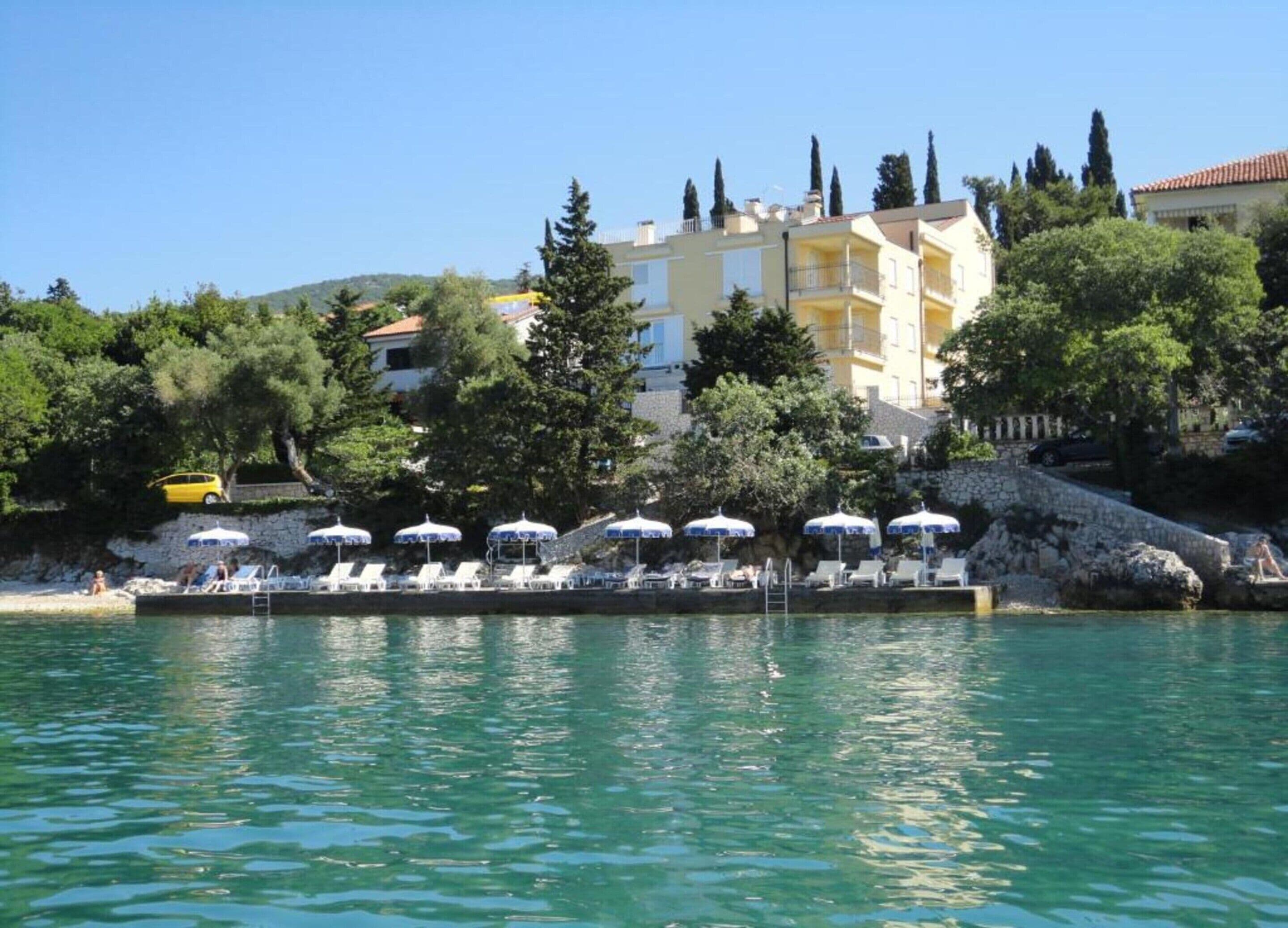 A waterfront hotel with outdoor swimming areas, sun loungers, and umbrellas.