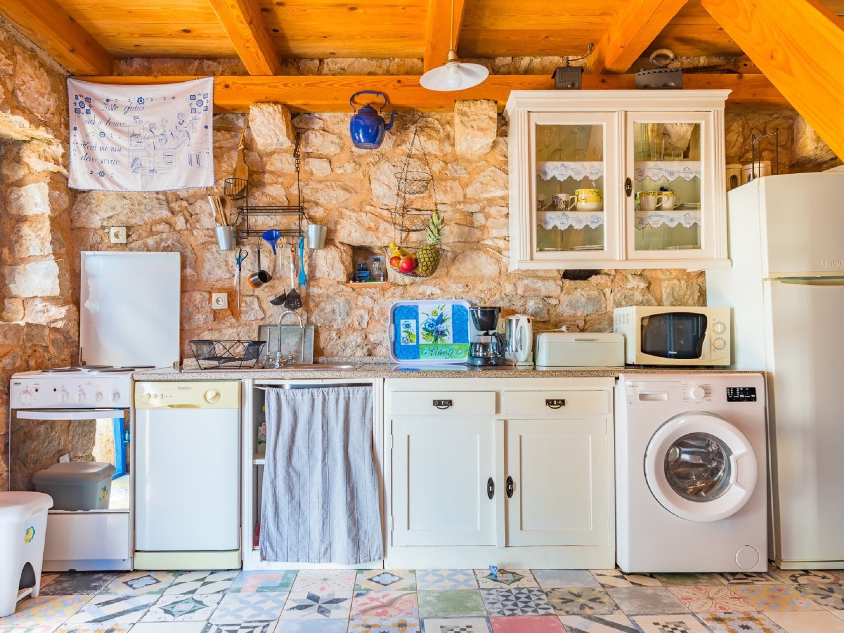 Una cucina rustica con pareti in pietra, travi in legno, una lavatrice, un forno a microonde e un fornello.