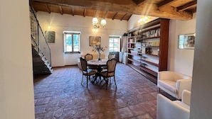 Ein Essbereich mit Steinboden, Holzbalkendecke, einer Chandelüster und einem Bücherregal.