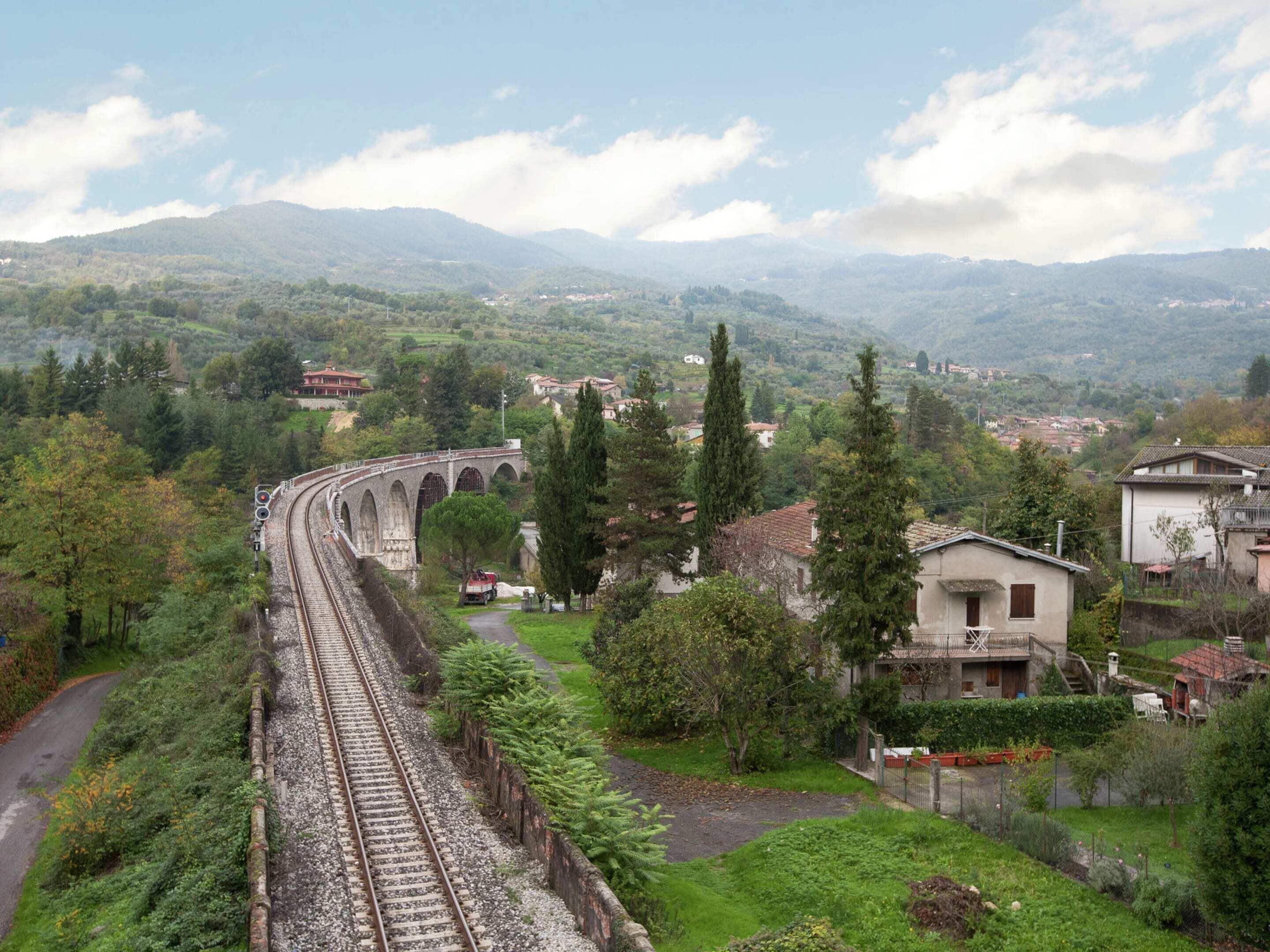 A railway track with a bridge, surrounded by greenery and houses.