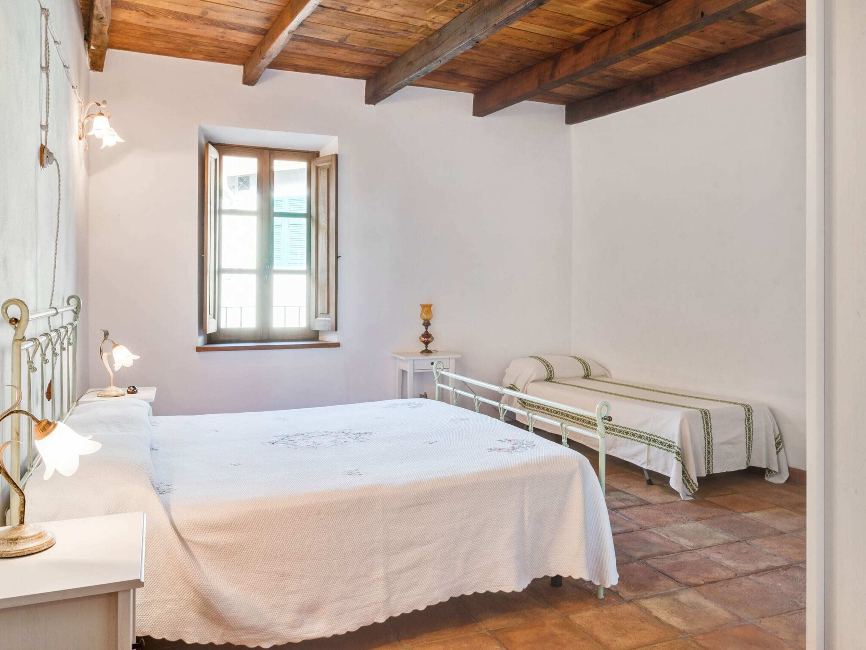 A bedroom with a bed, bedside table, lamp, window, and a bench.