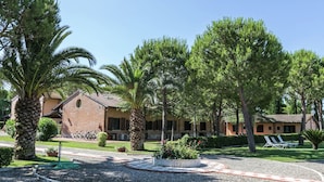A courtyard with palm trees, a brick building, and a gravel path. - Apartment Near the Beach and the Clear Blue Sea (Grosseto)