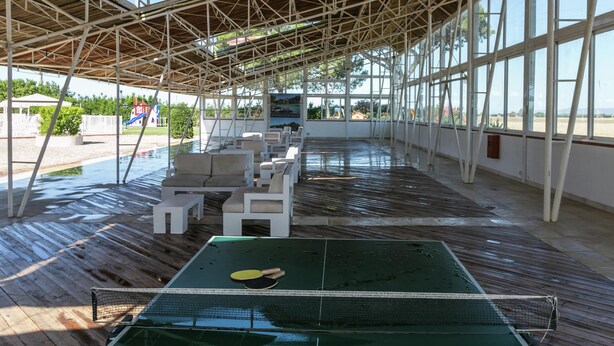 An indoor ping pong table with a net, surrounded by white cushioned chairs, under a wooden roof with large windows. - Apartment Near the Beach and the Clear Blue Sea (Grosseto)