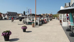 Ett offentligt torg med ett café, bänkar och planterade blommor och växter.
