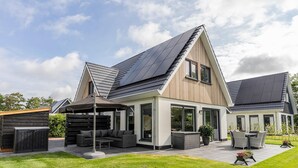 A modern house with a sloped roof, large windows, and a patio area with outdoor furniture. - Holiday Home in Texel Near the Sea (De Koog)