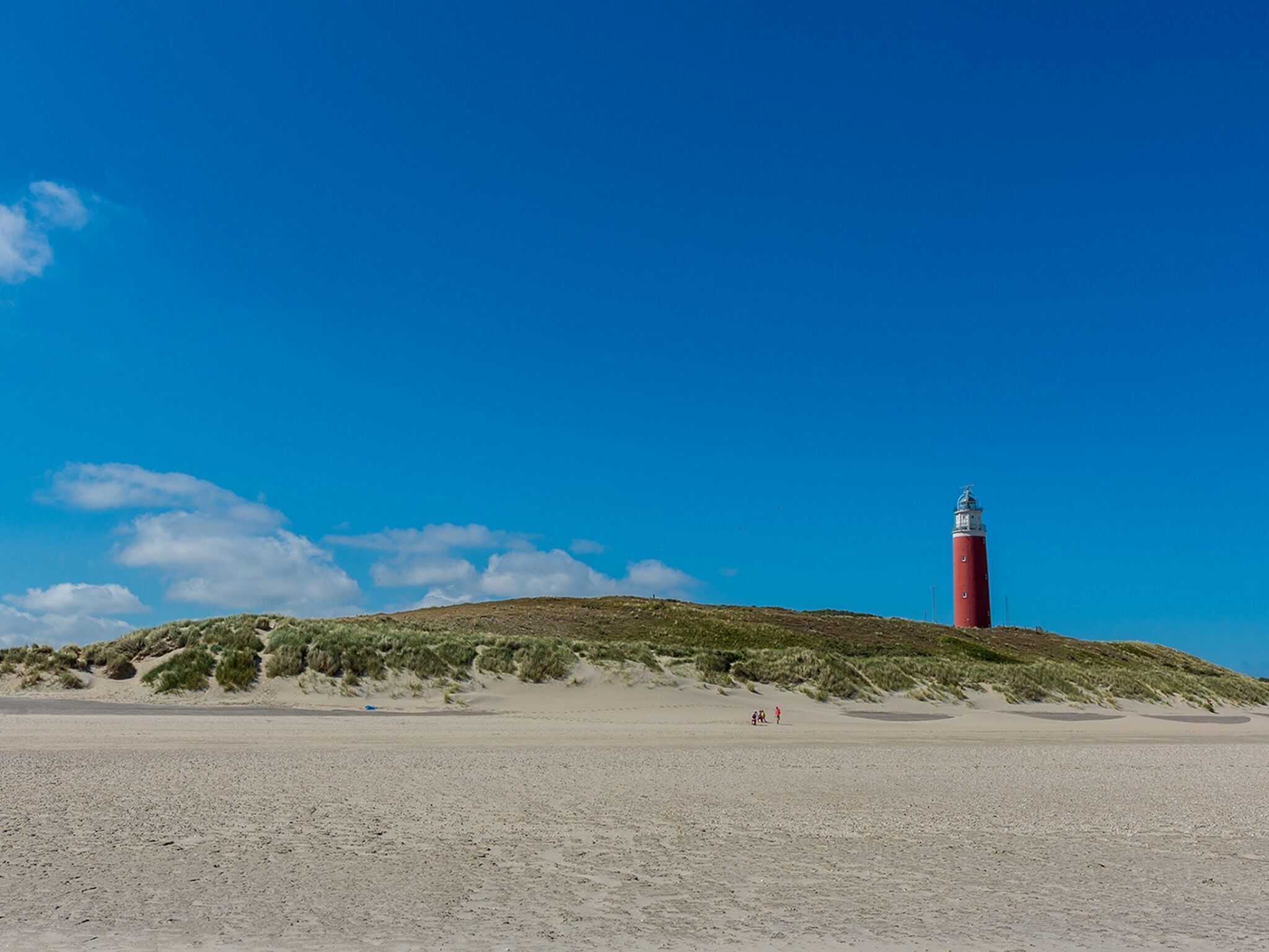 A lighthouse on a sandy beach with sparse vegetation.