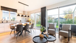 A modern kitchen with a dining area, large windows, and a view of the garden. - Holiday Home in Texel Near the Sea (De Koog)