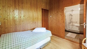 Ein Zimmer mit Holzwänden, einem Bett, einer Duschkabine und einer Tür zu einem anderen Raum.