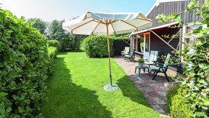 Ein gepflegter Garten mit einer Terrasse, die Gartenmöbel und einen großen Sonnenschirm bietet.