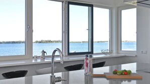 A modern kitchen with a large island, stainless steel sink, and a window overlooking a body of water. - Apartment in Kamperland by Veerse Meer Lake (Kamperland)