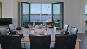 A dining area with a view of the water, a large window, and a table set for four. - Apartment in Kamperland by Veerse Meer Lake (Kamperland)