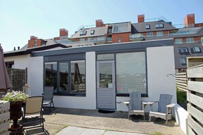 Una casa moderna con un patio que incluye un espacio de descanso con sillas y una mesa, y grandes ventanales con vistas al vecindario.