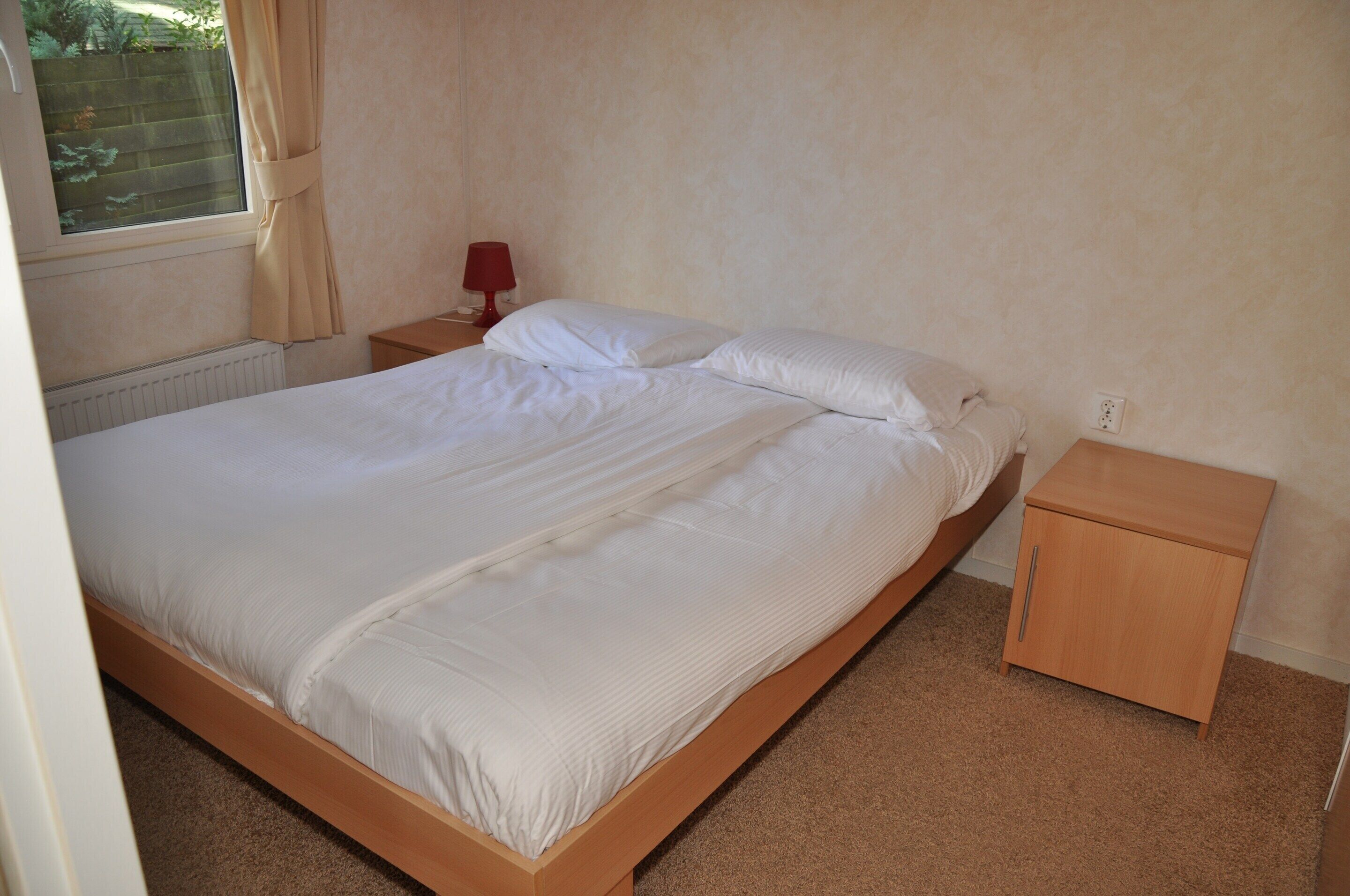 A single bed with a wooden frame, a nightstand with a lamp, and a small wooden cabinet.