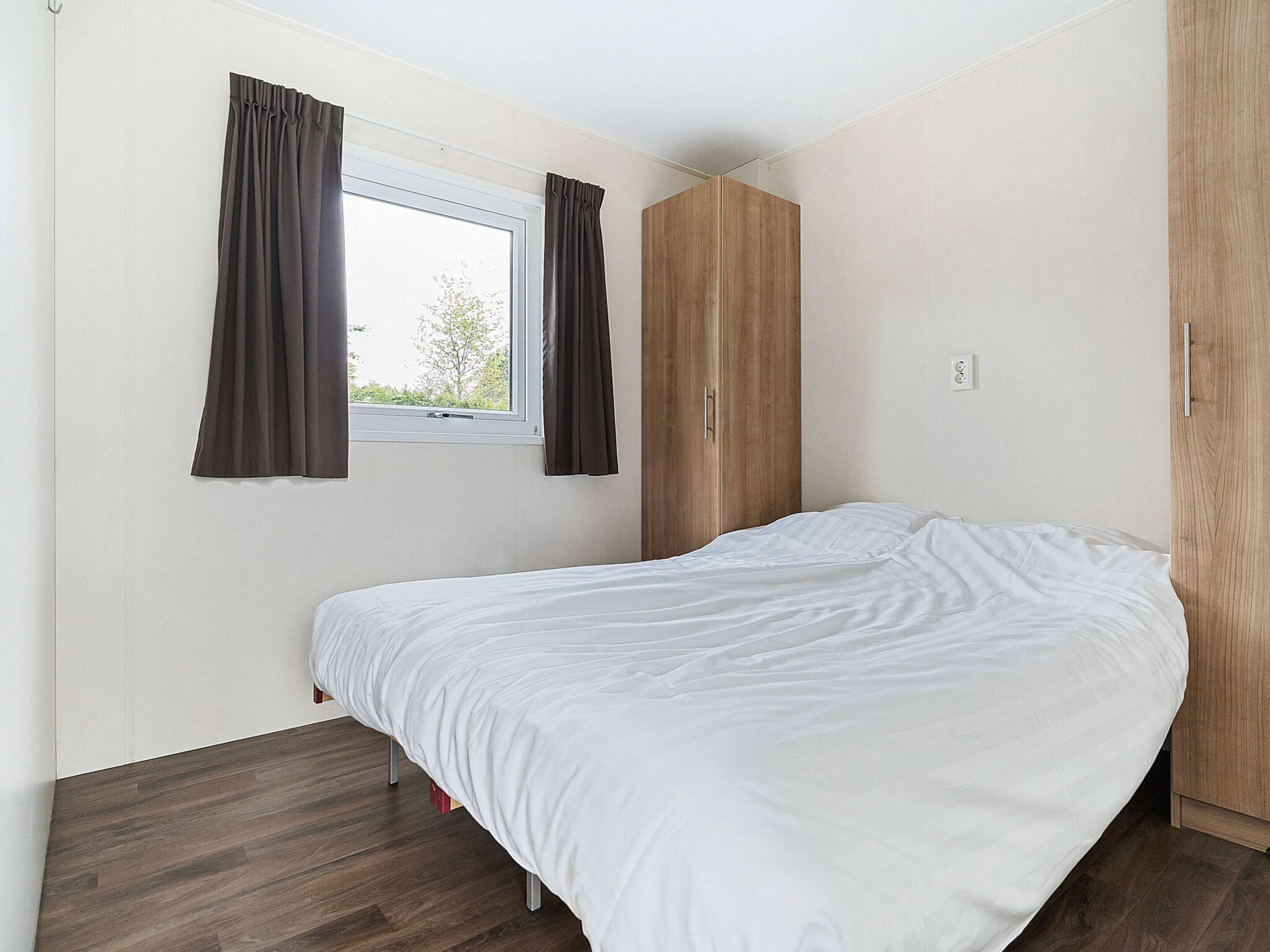 Een slaapkamer met een enkel bed, een raam met gordijnen, een kledingkast en een lichtschakelaar aan de muur.