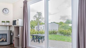 Une cuisine moderne équipée d’un four à micro-ondes, d’une horloge et d’une porte-fenêtre coulissante donnant sur une terrasse extérieure avec une table et des chaises.