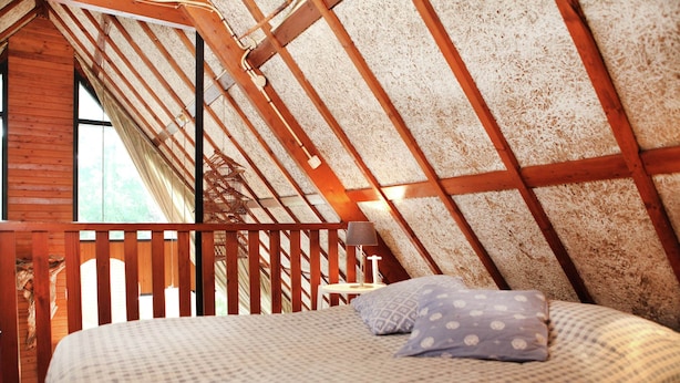 A bedroom with a sloped ceiling, wooden beams, a bed with patterned bedding, and a nightstand with a lamp. - Spacious Holiday Home in Eersel With Open Fire (Eersel)
