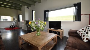 Een woonkamer met een houten salontafel, een televisie, een bank en een raam met gordijnen.