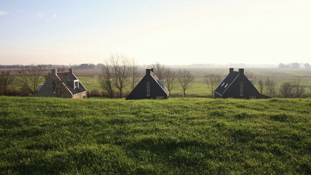 Drie huizen in een groen veld met een heldere lucht.