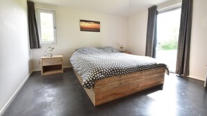 Een slaapkamer met een houten bed, een nachtkastje, een raam met gordijnen en een aan de muur bevestigd schilderij.