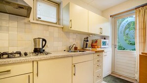 A kitchen with white cabinets, a gas stove, a coffee maker, a microwave, and a window with a view of greenery. - Apartment Noordwolde Rural Retreat (Noordwolde)