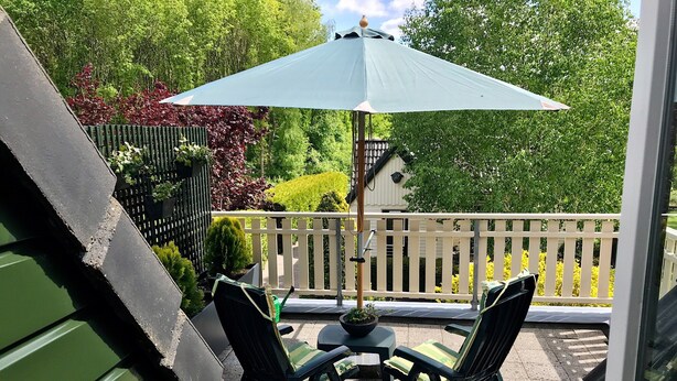 A patio with two chairs and a table, an umbrella, and a view of a white fence and greenery. - Apartment Noordwolde Rural Retreat (Noordwolde)