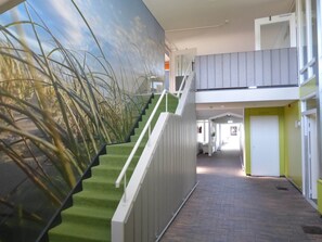 A staircase with green carpeted steps, white railings, and a wall mural of tall grasses.