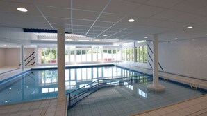 An indoor swimming pool with clear glass walls, white tiled floor, and ceiling lights. - Apartment in Hollum Near the Sea (Hollum)