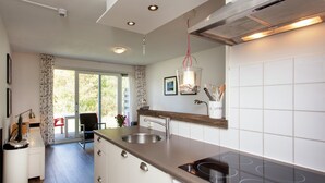 A modern kitchen with a built-in stove, a sink, and a dining area with a chair and table. - Apartment in Hollum Near the Sea (Hollum)